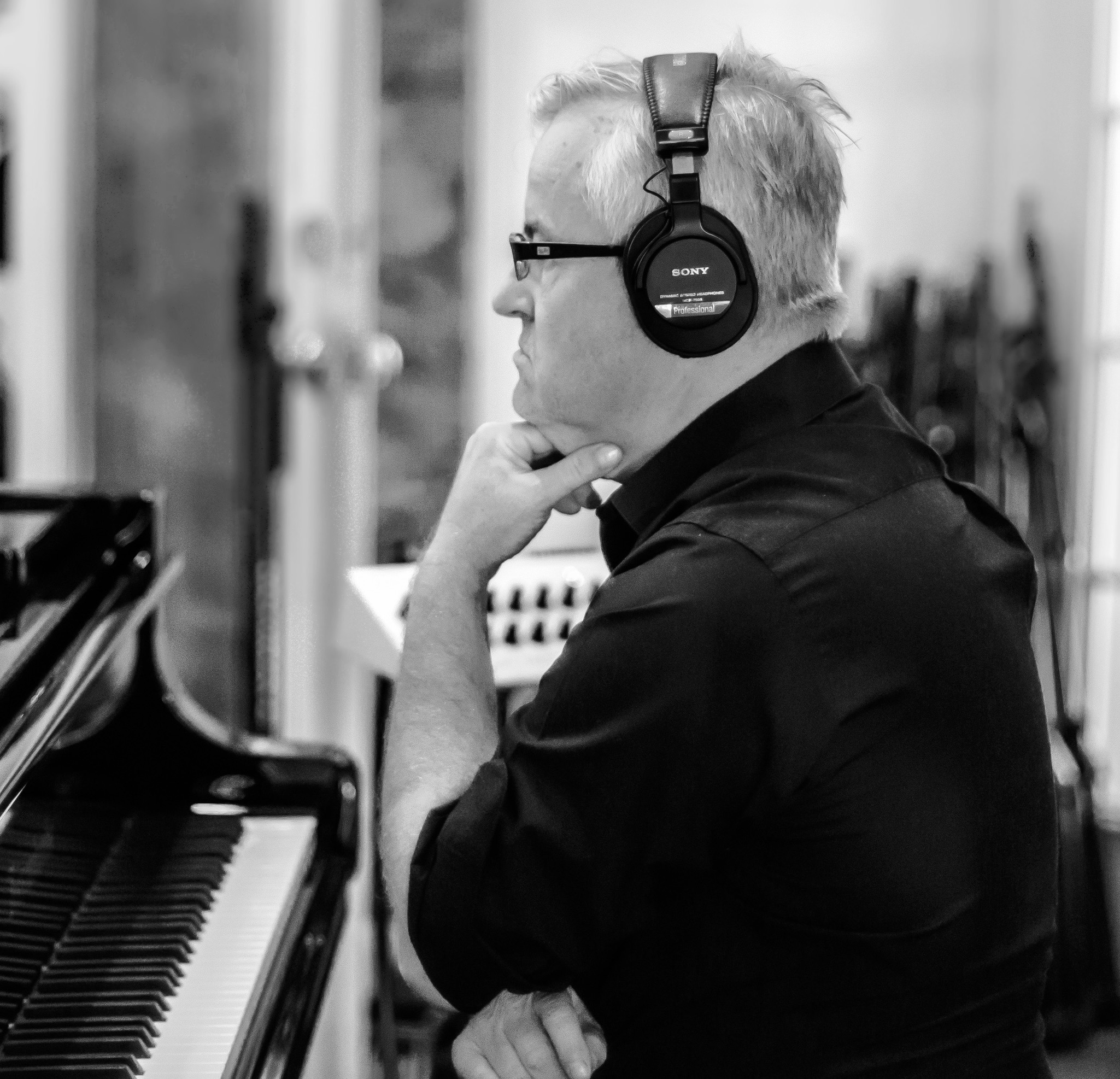 Markus Burger listening through headphones beside a piano in the recording studio